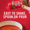 ['A hand holds a McCormick Crushed Red Pepper &amp; Italian Herbs Seasoning bottle over a bowl of tomato soup.']