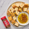 ['A plate of toasted bread cubes with a side of olive oil and McCormick Crushed Red Pepper &amp; Italian Herbs Seasoning.']