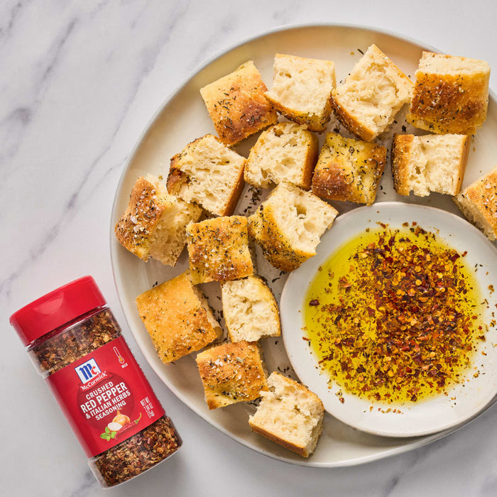 ['A plate of toasted bread cubes with a side of olive oil and McCormick Crushed Red Pepper &amp; Italian Herbs Seasoning.']