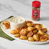 ['A plate of crispy roasted potatoes with a side of sour cream and a jar of McCormick Red &amp; Green Pepper Blend.']