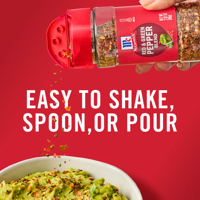 ['A hand holding a McCormick Red &amp; Green Pepper Blend shaker, with red pepper flakes falling into a bowl of guacamole.']