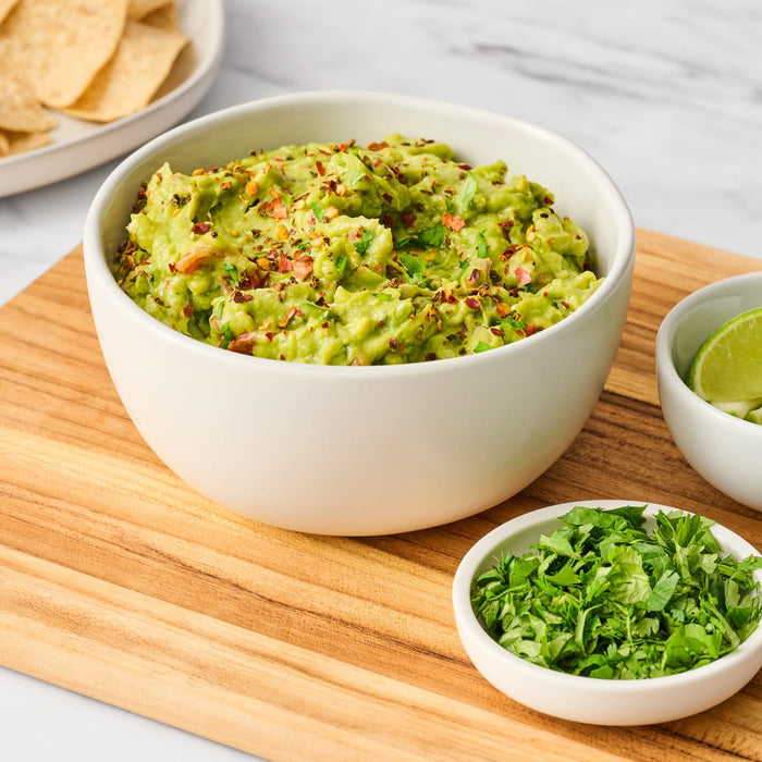 ['A bowl of guacamole with tortilla chips, lime wedges, and cilantro on a wooden cutting board.']