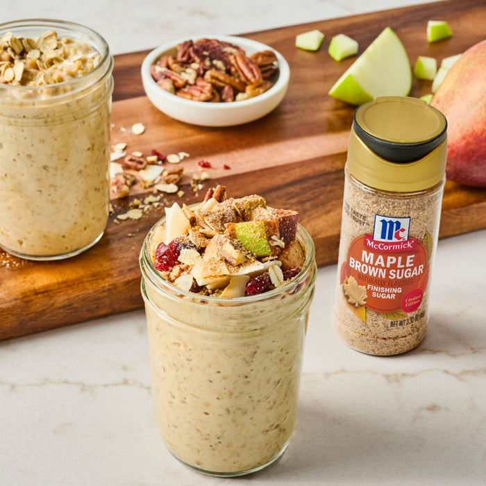 A jar of overnight oats with apple, cranberries, and pecans, alongside a jar of McCormick Maple Butter Seasoning.