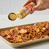 A hand sprinkles Great Value brand seasoning onto a tray of snack mix.