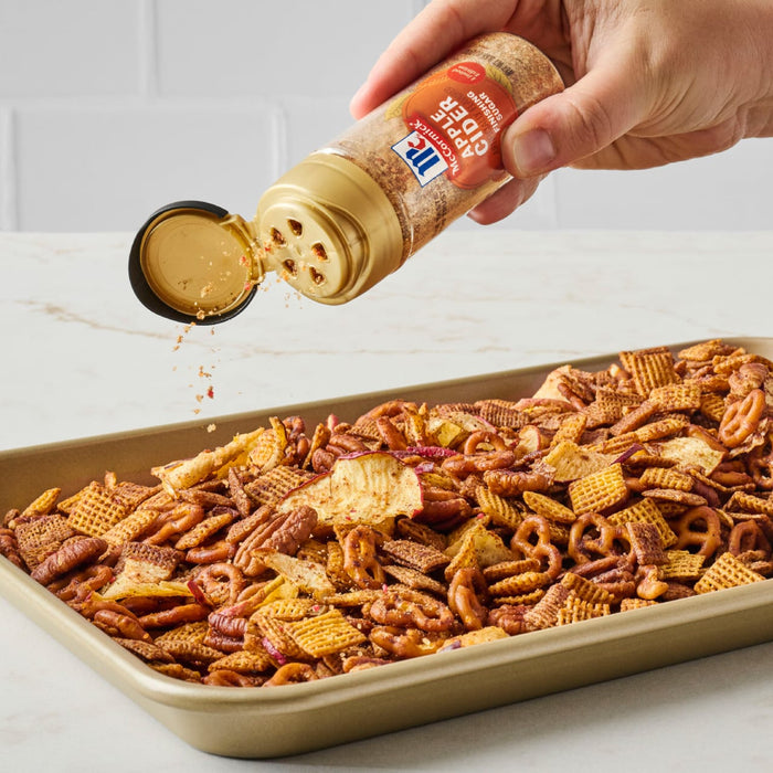 A hand sprinkles Great Value brand seasoning onto a tray of snack mix.