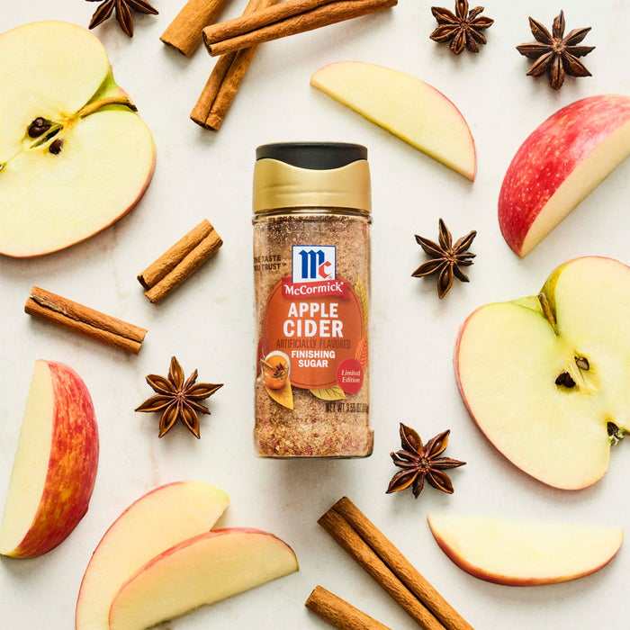 A bottle of McCormick Apple Cider spice blend is surrounded by apple slices, cinnamon sticks, and star anise.