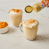 Two mugs of pumpkin spice lattes are being sprinkled with McCormick Pumpkin Pie Spice.