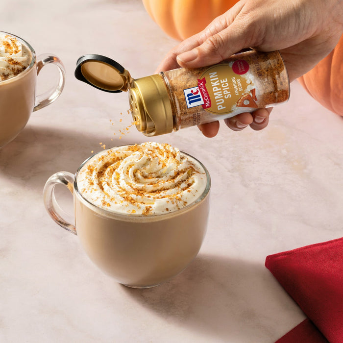 Two mugs of pumpkin spice lattes are being sprinkled with McCormick Pumpkin Pie Spice.