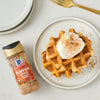 A plate of waffles topped with cream and McCormick Pumpkin Spice Seasoning sits next to a bottle of the seasoning.