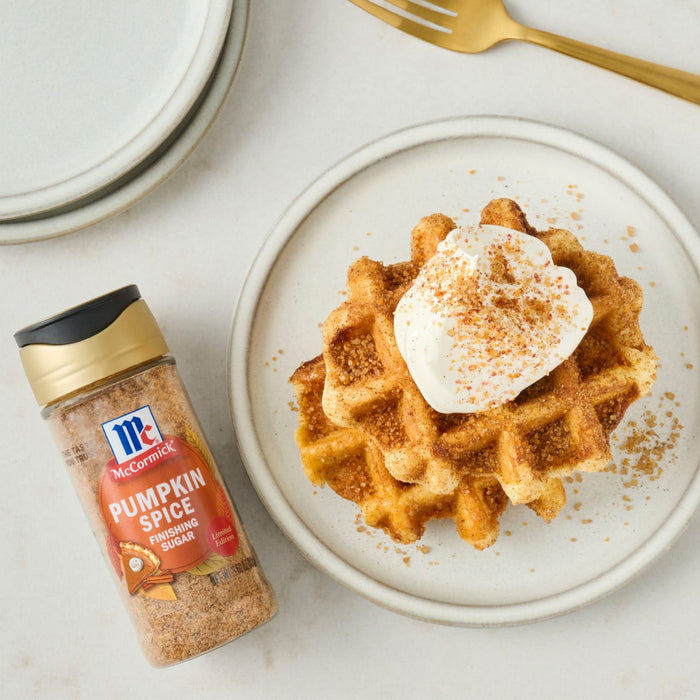 A plate of waffles topped with cream and McCormick Pumpkin Spice Seasoning sits next to a bottle of the seasoning.