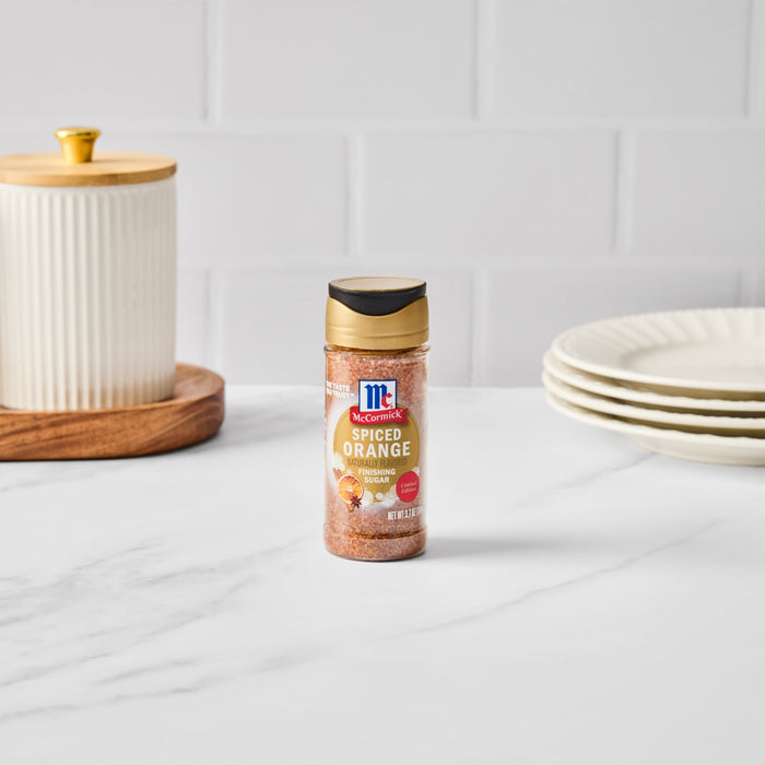 A bottle of McCormick Pumpkin Spice seasoning sits on a white countertop next to a decorative jar and stack of plates.