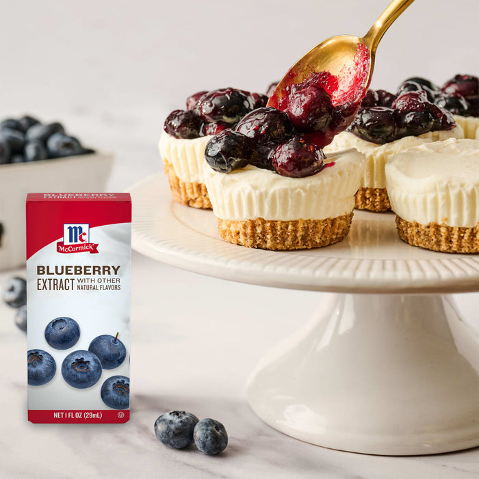 A box of McCormick Blueberry Extract is displayed next to mini cheesecakes topped with blueberries being drizzled with a blueberry sauce.