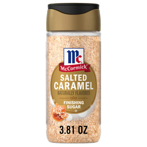 A clear glass shaker bottle containing Mccormick Salted Caramel Fin Sgr 3.81 Oz, a light brown finishing sugar, with a gold and black cap and an orange label displaying the McCormick logo.