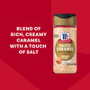 A bottle of Mccormick Salted Caramel Fin Sgr 3.81 Oz, a bowl of the sugar, and a hand rimming a glass, with a finished apple drink in the background, emphasizing its role as a perfect finishing touch.
