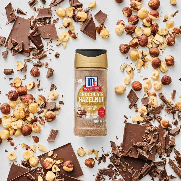 A bottle of McCormick Chocolate Hazelnut Flavored Seasoning is surrounded by chocolate pieces and hazelnuts.