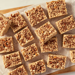 A tray of pretzel and white chocolate dessert bars sits next to bowls of pretzels and peanuts.