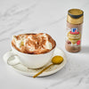 A cup of hot chocolate with whipped cream and McCormick Hazelnut topping sits next to a bottle of the topping.