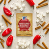 A packet of McCormick Sweet &amp; Spicy Holiday Party Mix is surrounded by sugar cubes, cinnamon sticks, and red peppers.