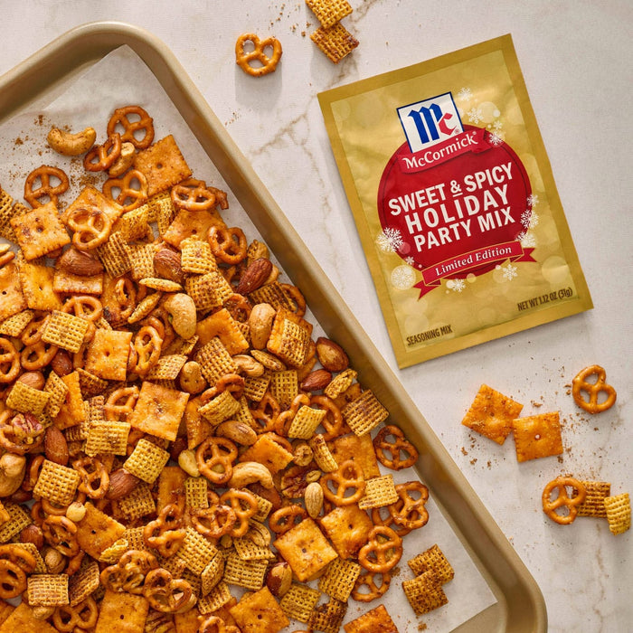 A tray of homemade party mix with pretzels, cheese crackers, and peanuts, next to a packet of McCormick Sweet &amp; Spicy Holiday Party Mix seasoning.