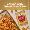 A McCormick Sweet &amp; Spicy Holiday Party Mix packet is displayed next to a baking sheet filled with a homemade snack mix of pretzels, nuts, and crackers, promoting an easy, giftable snack mix.