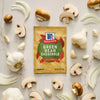A packet of McCormick Green Bean Casserole seasoning mix is surrounded by fresh mushrooms, garlic cloves, and onion slices.