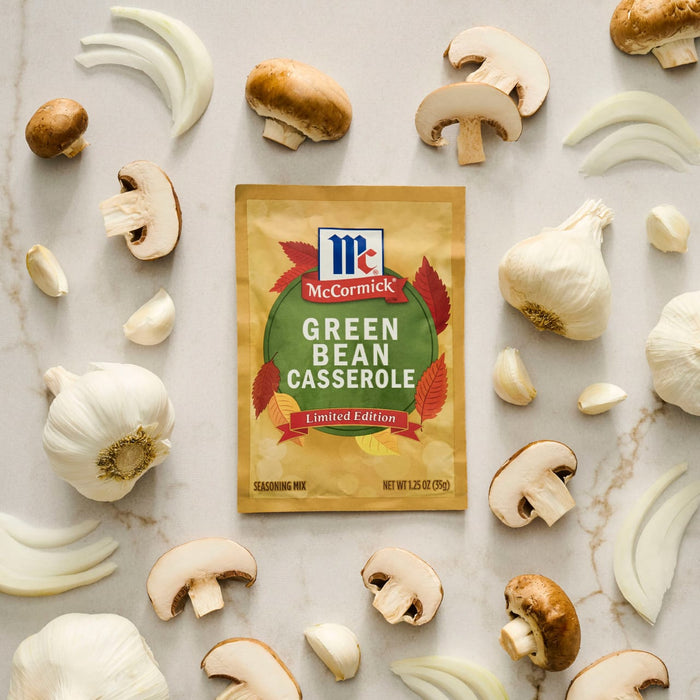 A packet of McCormick Green Bean Casserole seasoning mix is surrounded by fresh mushrooms, garlic cloves, and onion slices.