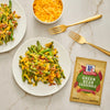 Two plates of green bean casserole with McCormick Green Bean Casserole seasoning packet and a bowl of shredded cheese.