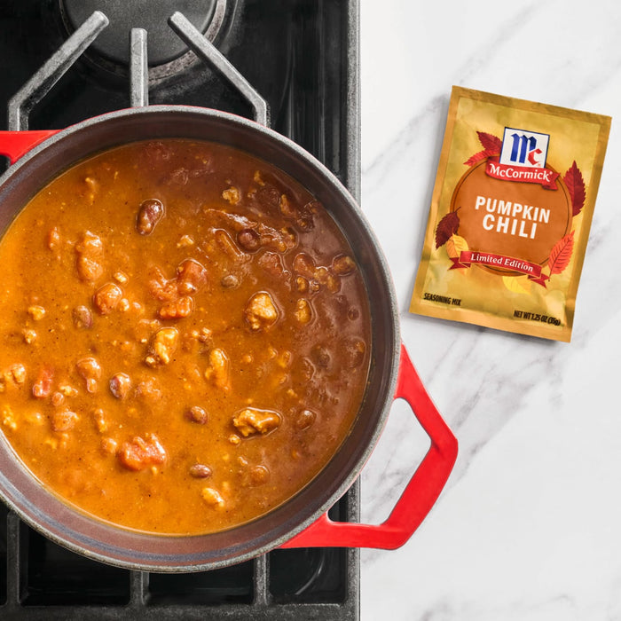 A pot of pumpkin chili simmers on the stove next to a packet of McCormick Pumpkin Chili seasoning.