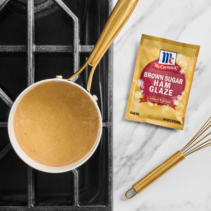 A packet of McCormick Brown Sugar Ham Glaze is displayed next to a saucepan of glaze and a whisk.