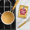 A packet of McCormick Brown Sugar Ham Glaze is displayed next to a saucepan of glaze and a whisk.