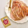 A glazed spiral ham on a plate with a McCormick Brown Sugar Ham Glaze packet.