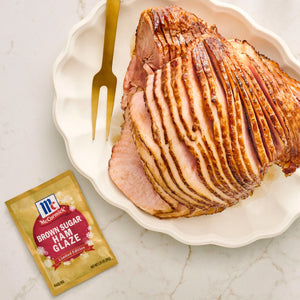 A glazed spiral ham on a plate with a McCormick Brown Sugar Ham Glaze packet.