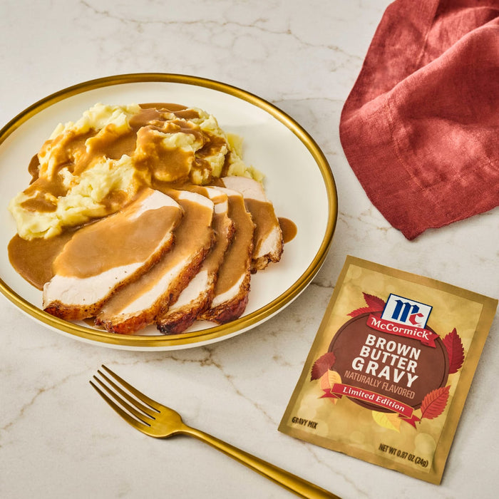 A plate of sliced turkey and mashed potatoes covered in McCormick Brown Gravy, next to a packet of the gravy mix.