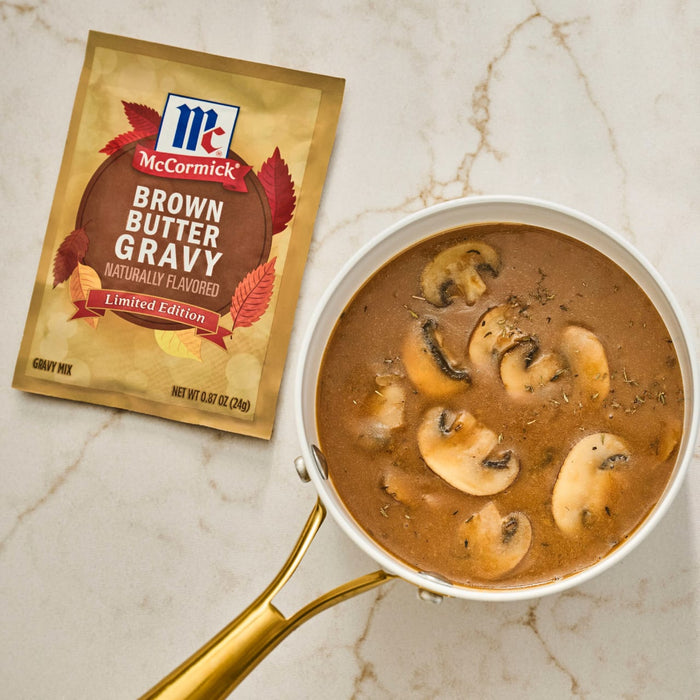 A packet of McCormick Brown Butter Gravy mix sits next to a saucepan filled with gravy and sliced mushrooms.