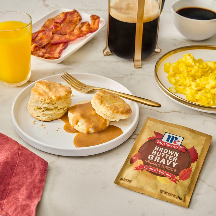 A breakfast spread featuring McCormick Brown Butter Gravy with biscuits, bacon, eggs, and orange juice.