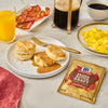 A breakfast spread featuring McCormick Brown Butter Gravy with biscuits, bacon, eggs, and orange juice.