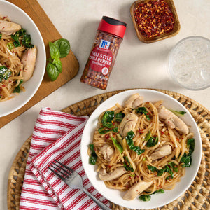 A bowl of Thai style chili pepper chicken noodles with a McCormick Thai Style Chili Pepper bottle on the table.
