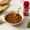A bowl of Thai style chili pepper sauce with McCormick Thai Style Chili Pepper Crushed bottle lime slices and parsley on a table.