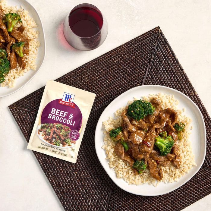A plate of beef and broccoli with rice a glass of red wine and a McCormick Beef &amp; Broccoli seasoning mix packet are displayed on a woven placemat.