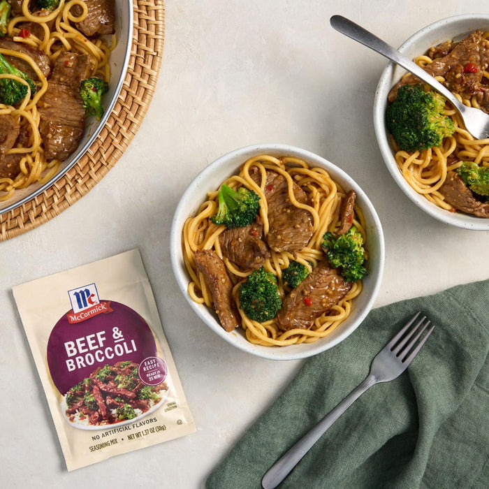 This is a photo of McCormick Beef &amp; Broccoli seasoning mix with bowls of beef and broccoli noodles.