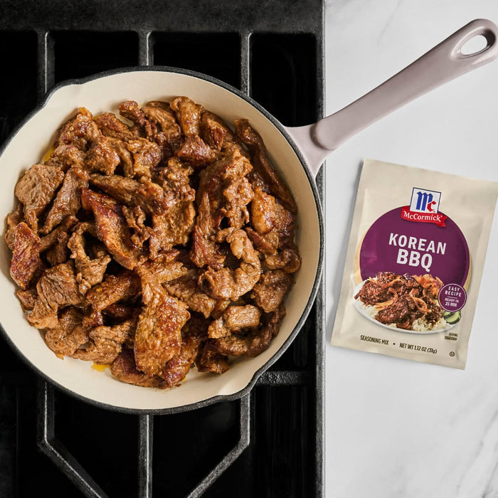 A pan of Korean BBQ beef made with McCormick seasoning mix sits on a stove top next to the seasoning packet.