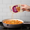 A hand pours McCormick Butter Chicken seasoning into a pan of butter chicken.