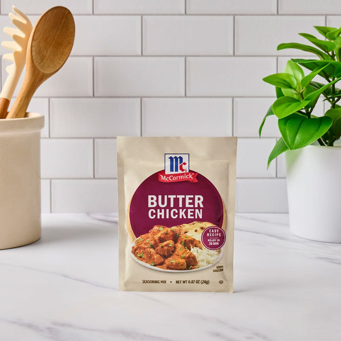 A packet of McCormick Butter Chicken seasoning mix sits on a marble countertop next to a plant and a utensil holder.