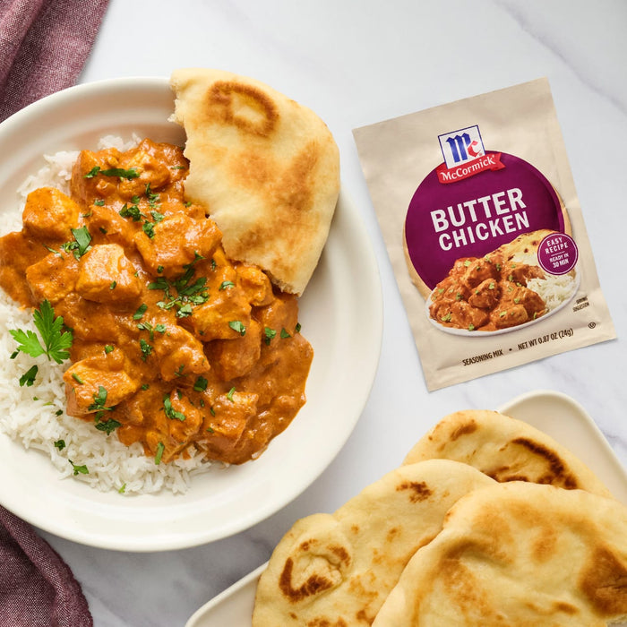 A bowl of butter chicken and rice with naan bread alongside a McCormick Butter Chicken seasoning mix packet.