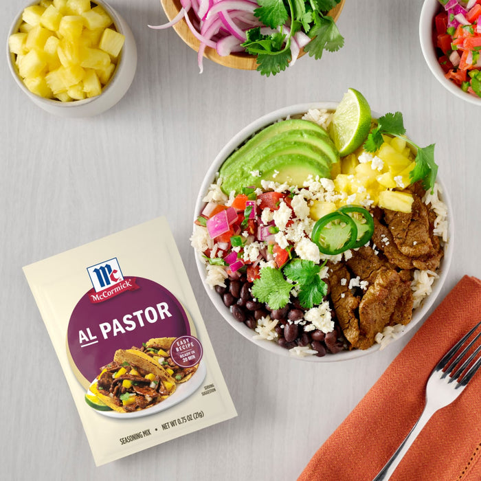 A McCormick Al Pastor seasoning mix packet is displayed next to a bowl of Al Pastor tacos with rice beans avocado and pineapple.