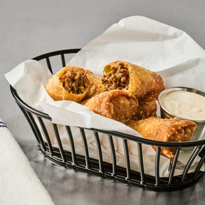 A basket of crispy fried egg rolls with a side of dipping sauce.
