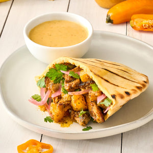 A grilled pita bread filled with chicken onions and cilantro is served on a white plate with a side of dipping sauce.