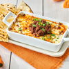 A white baking dish filled with a cheesy dip topped with ground meat and cilantro served with tortilla chips.