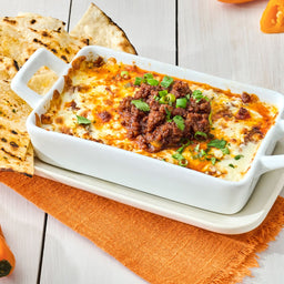 A white baking dish filled with a cheesy dip topped with ground meat and cilantro served with tortilla chips.