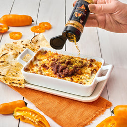 A hand sprinkles Flavor the Year Aji Amarillo seasoning on a dish of cheesy dip with tortilla chips and orange peppers.